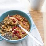 Buckwheat Pumpkin Power Bowl topped with chia seeds, dried cranberries, apples and pecans served in a light blue bowl on white dish towel.
