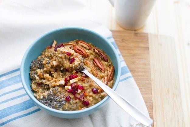 Buckwheat Pumpkin Power Bowl topped with chia seeds, dried cranberries, apples and pecans served in a light blue bowl on white dish towel.
