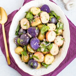 Tri-colored potato salad with shallots and spinach in a white bowl with a purple napkin and gold spoon.