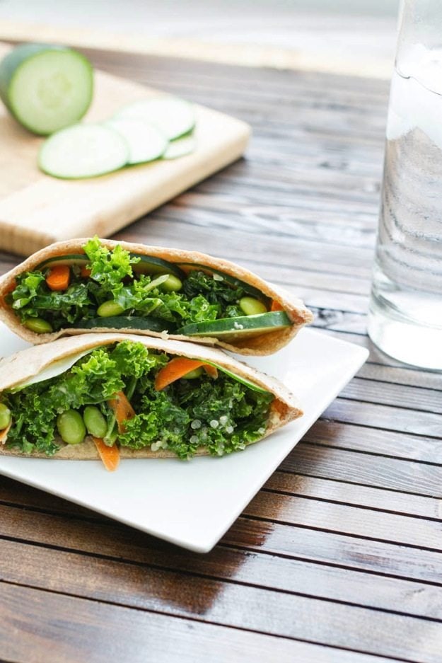 Kale Salad Stuffed Pitas served on a white square plate on wood table with glass of water.