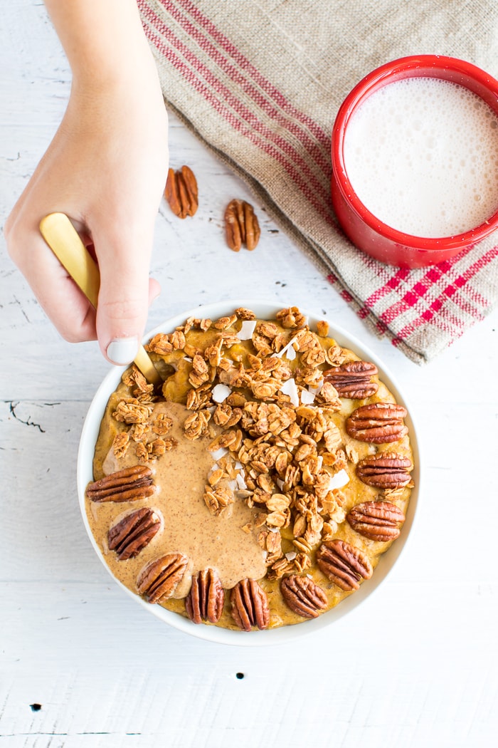 Hand taking a spoonful fo protein pumpkin oatmeal. A mug of almond milk is to the side.