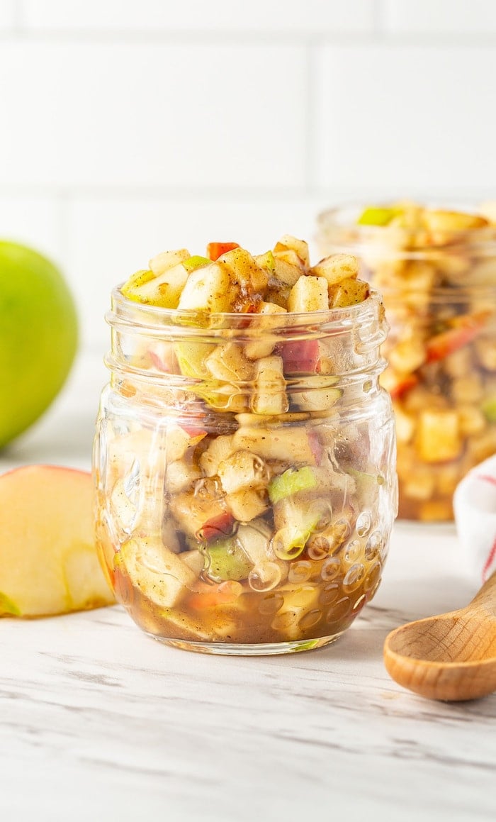 Straight on image of raw apple pie filling a glass jar.