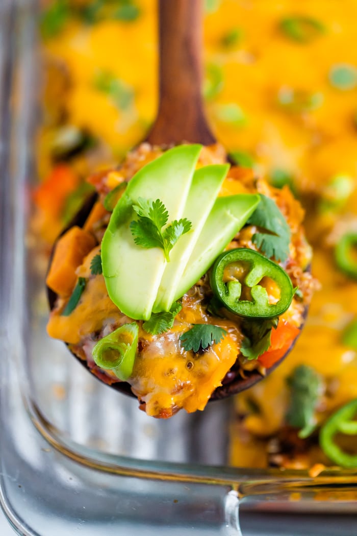 Wood serving spoon scooping up a serving of cheesy healthy Mexican quinoa casserole topped with avocado.