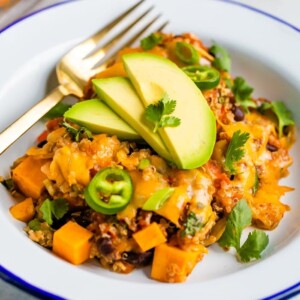 Plate with a cheesy Mexican quinoa casserole topped with jalapenos slices, avocado, and cilantro.