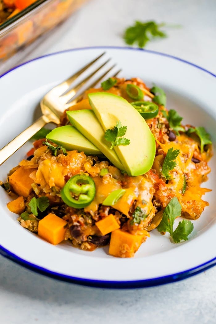 Plate with a cheesy Mexican quinoa casserole topped with jalapenos slices, avocado, and cilantro.