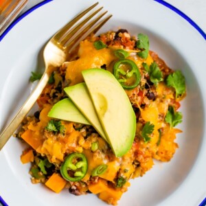 Plate and fork with a portion of a Mexican quinoa casserole topped with avocado and cilantro.