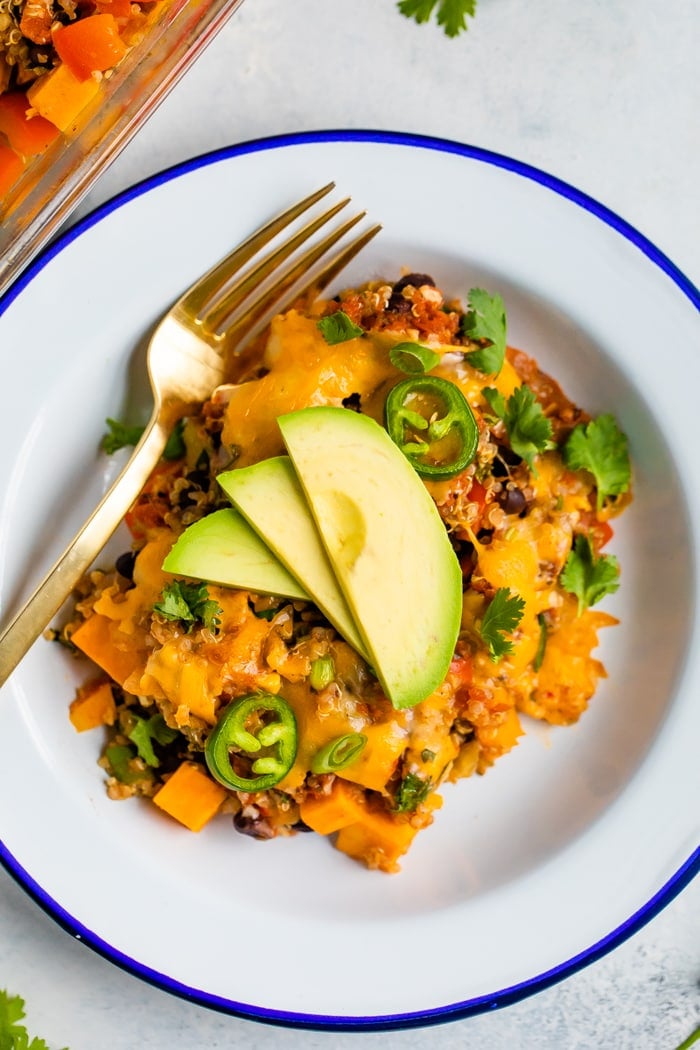 Plate and fork with a portion of a Mexican quinoa casserole topped with avocado and cilantro.