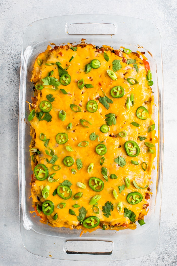 Casserole dish of a Mexican Quinoa Casserole topped with lots of cheddar cheese, green onions, cilantro, and jalapeno slices.