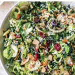 Kale and brussels sprout salad in a serving bowl topped with dried cranberries, almonds and cheese.