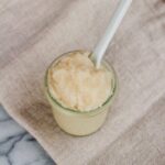 Small jar of homemade whipped coconut oil sugar scrub with a spoon handling sticking out of the jar.