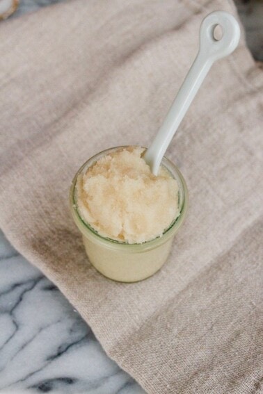 Small jar of homemade whipped coconut oil sugar scrub with a spoon handling sticking out of the jar.