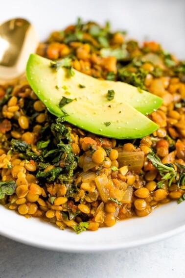 Close up of thick lentil stew with kale and topped with avocado slices.