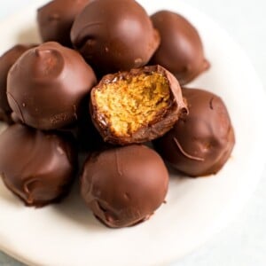 Plate of healthy peanut butter balls covered in chocolate. One has bite taken out of it.