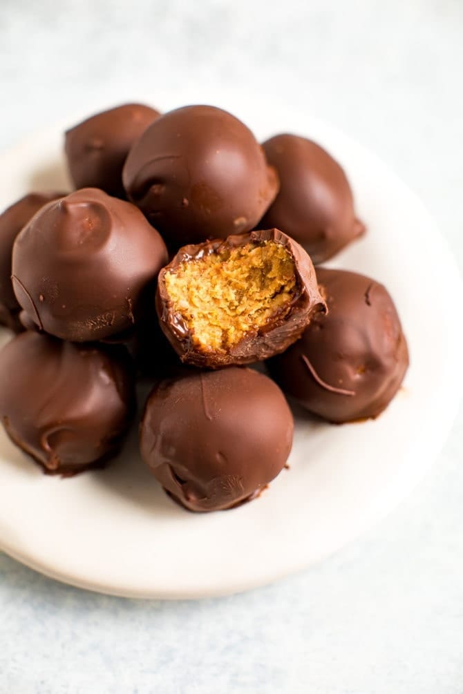 Chocolate covered peanut butter balls on a plate. One has a bite taken out of it.