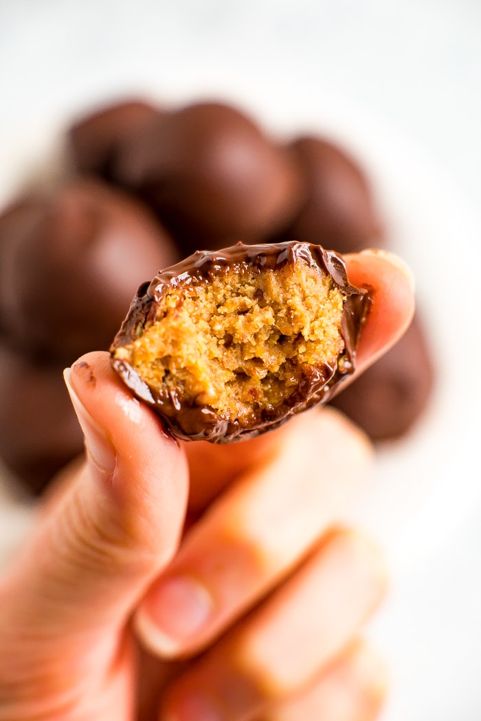 Hand holding a healthy peanut butter ball covered in chocolate with a bite taken out of it.