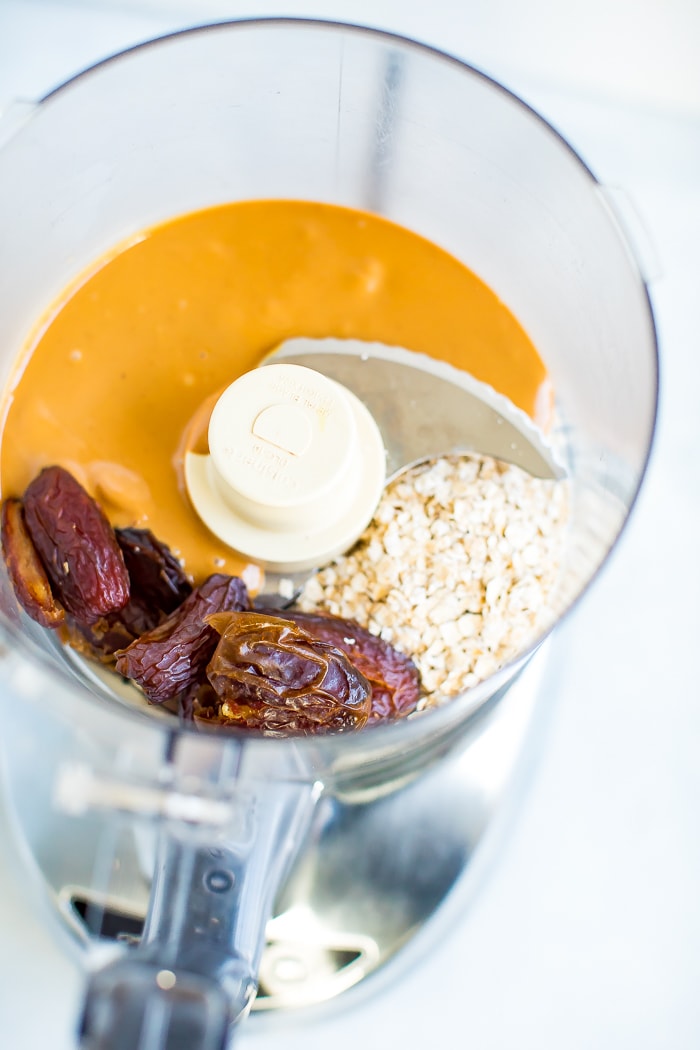 Food processor with the ingredients for healthy peanut butter balls-- peanut butter, dates, and oatmeal.