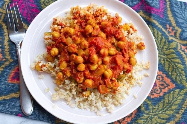 Channa Masala served with brown rice on white plate and colorful placemat.