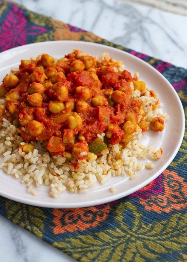 Channa Masala served with brown rice on white plate and colorful placemat.