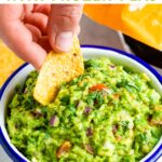 Hand dipping a tortilla chip into a bowl of guacamole.