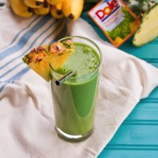 Vitamin C Booster Green Smoothie served in a tall clear class with slice of pineapple.