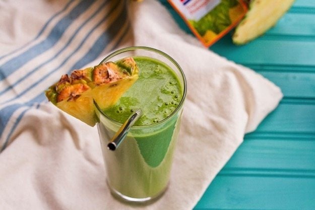 Vitamin C Booster Green Smoothie served in a tall clear class with slice of pineapple. 