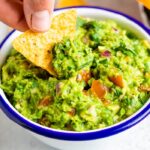 Hand dipping a tortilla chip into a bowl of guacamole.