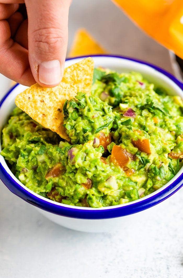 Hand dipping a tortilla chip into a bowl of guacamole.