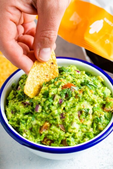 Hand dipping a chip into a bowl of frozen pea guacamole.