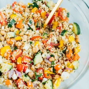 Quinoa chickpea salad in a large clear glass bowl with a gold spoon.