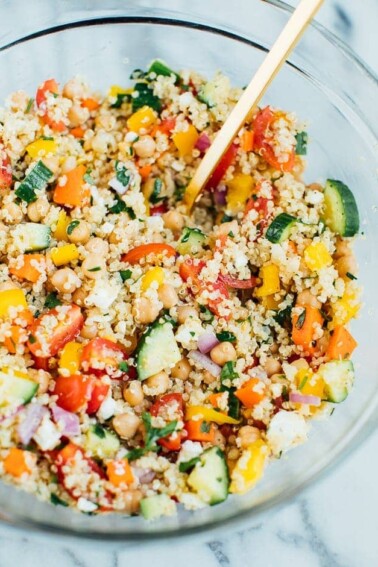 Quinoa chickpea salad in a large clear glass bowl with a gold spoon.