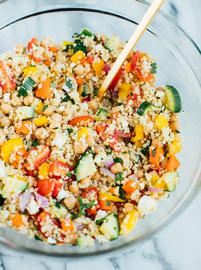 Quinoa chickpea salad in a large clear glass bowl with a gold spoon. 