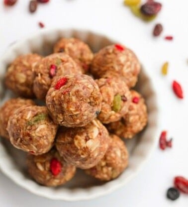 White bowl of Superfood Energy Balls with scattered superfood berries around the perimeter.