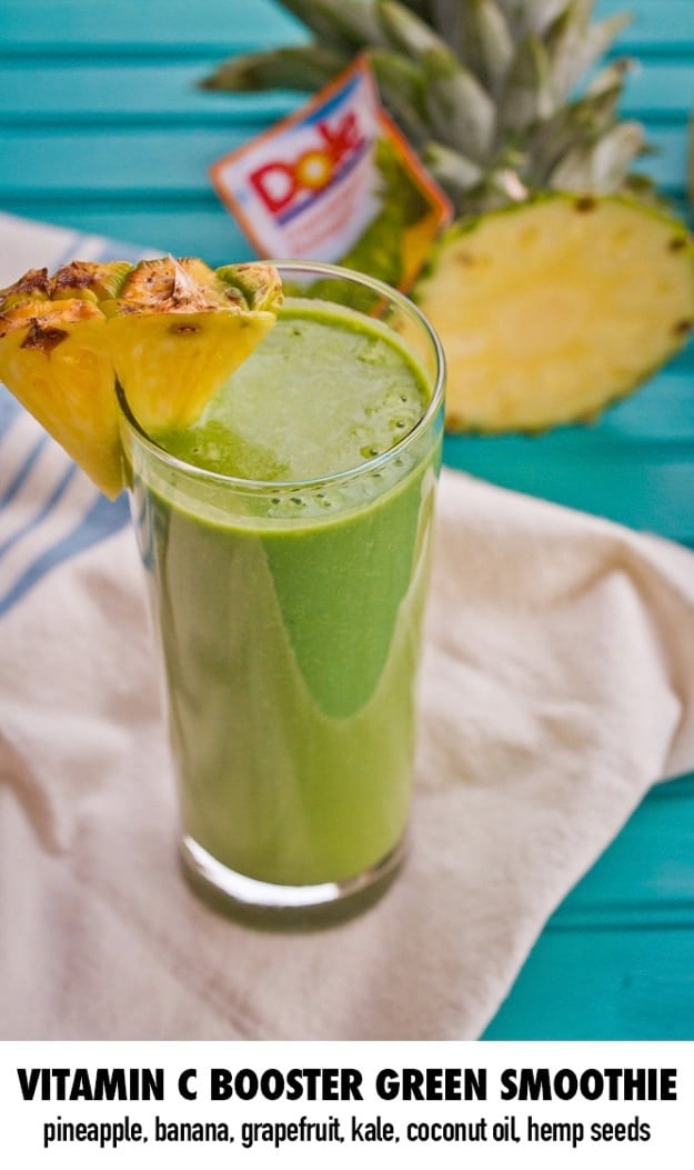 Vitamin C Booster Green Smoothie served in a tall clear class with slice of pineapple. 
