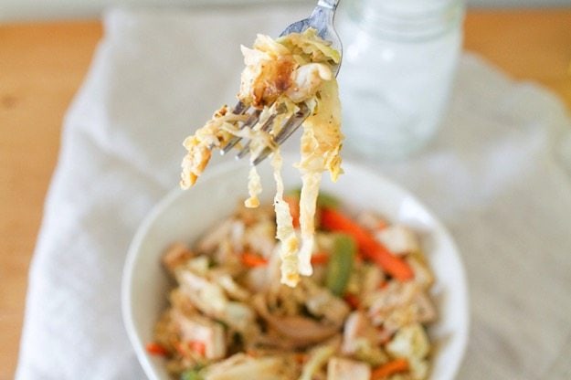 A fork holding up a bite of tofu cabbage noodles. A bowl is below the fork.