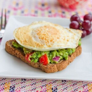 A fried egg resting on top of a slice of toast with spread with guacamole.