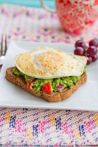 A fried egg resting on top of a slice of toast with spread with guacamole.