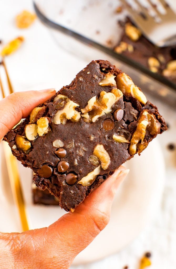 hand holding a flourless black bean brownie topped with walnuts and chocolate chips