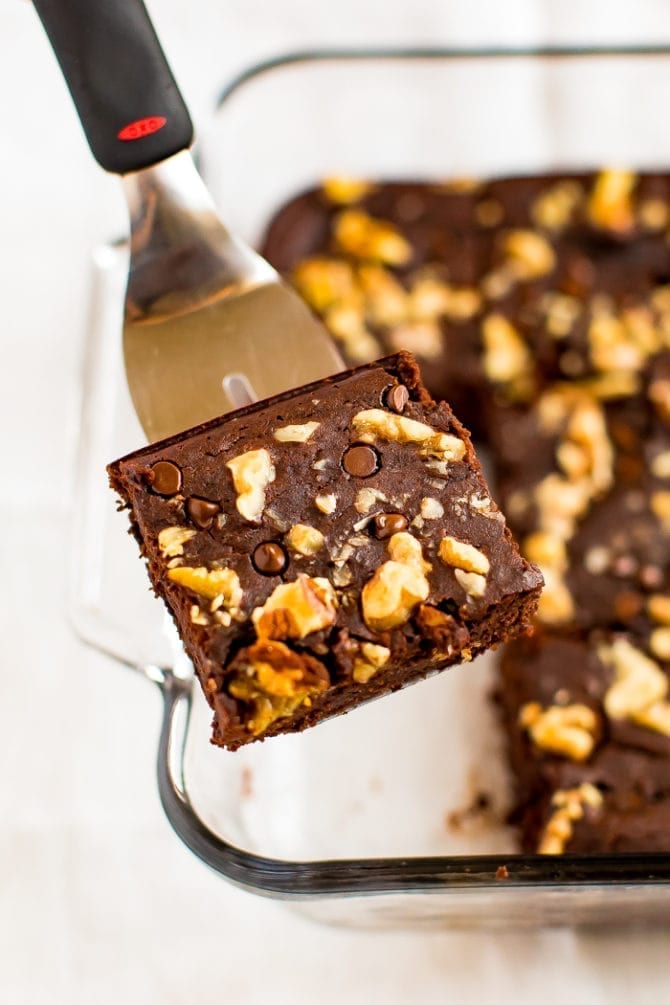 Spatula lifting a black bean brownie topped with walnuts and chocolate chips from a pan.