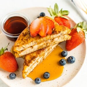 Banana and almond butter stuffed french toast on a plate with berries and topped with maple syrup.