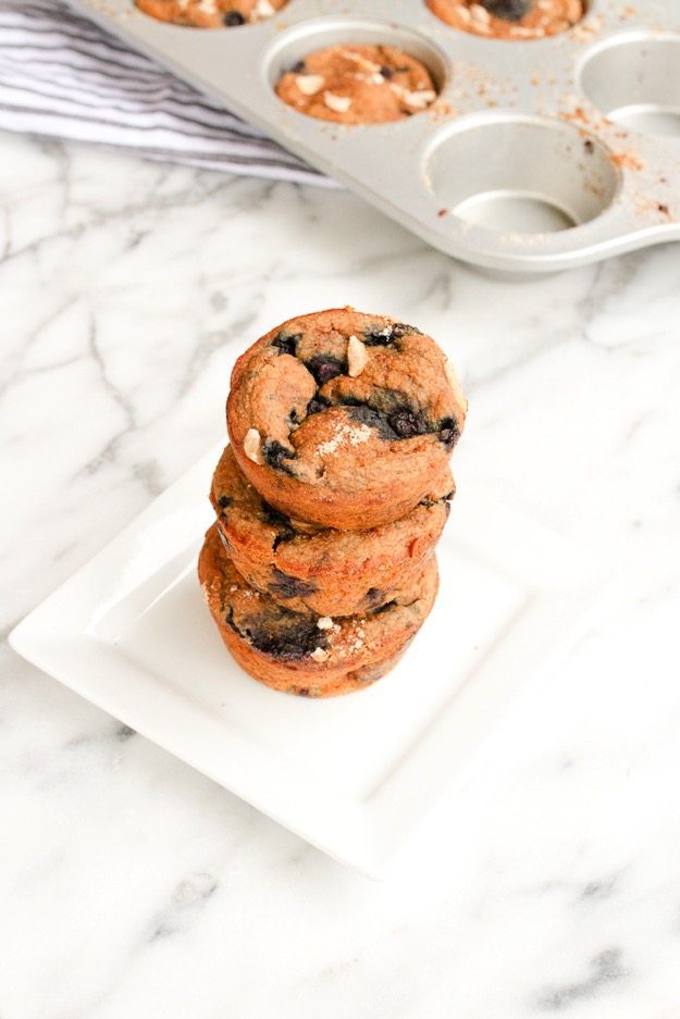 Stack of 3 protein blueberry almond muffins on a square plate. Muffin tin in the background.