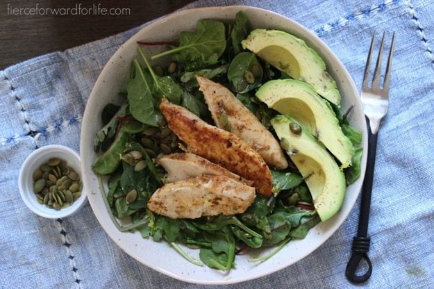 Power Greens Salad + Citrus Dressing in white shallow bowl with pumpkin seeds and a fork on the side.