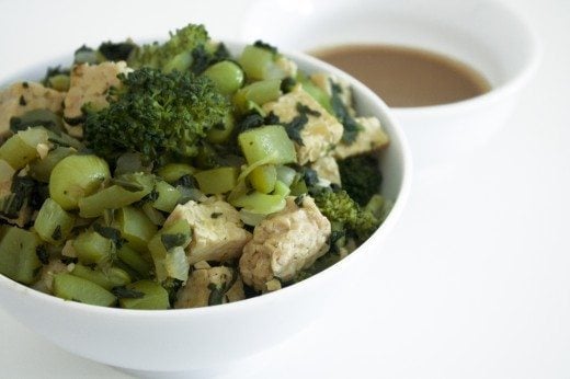 Tempeh & Green Vegetables with Tangy Peanut Sauce in white bowl on white counter.