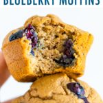 Hand holding two blueberry muffins. One has a bite taken out of it.