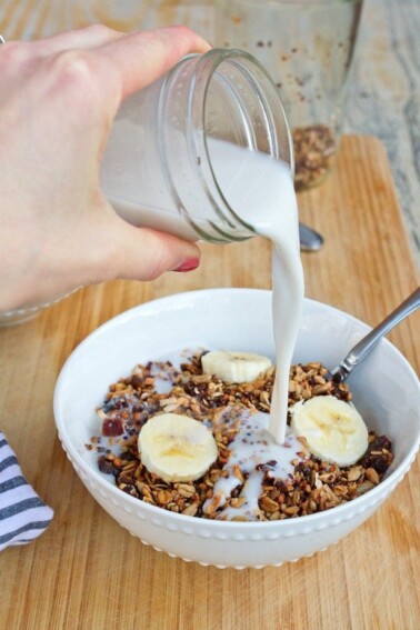 Homemade Gluten-free Cereal with Quinoa Buckwheat & Dates in a bowl with milk being poured into the bowl from a mason jar.