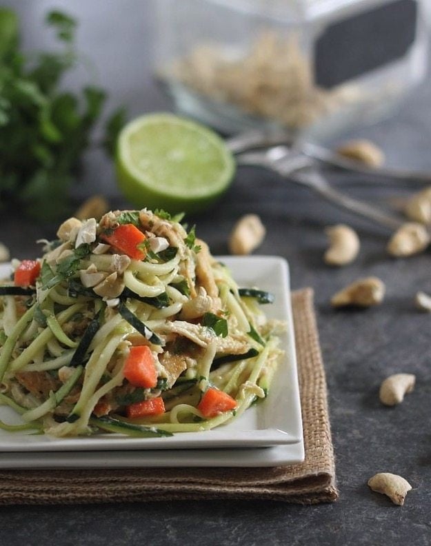Thai Chicken Zucchini Noodles by Running to the Kitchen Thai Chicken Zucchini Noodles on a white square plate. Lime, cashews, and herbs in the background.