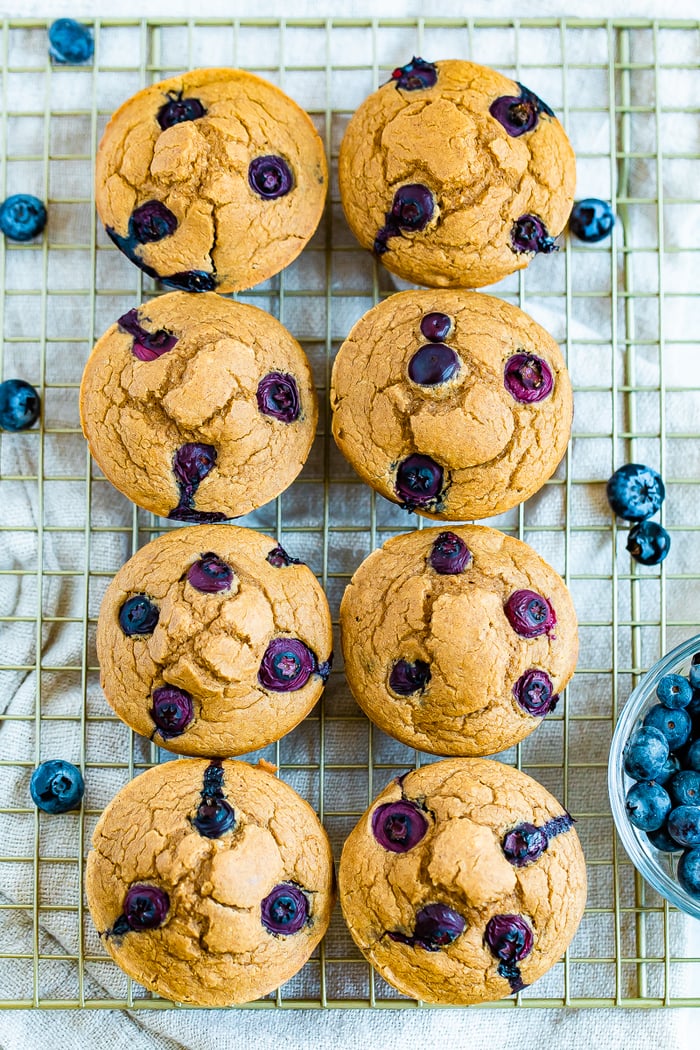 Eight blueberry muffins on a cooling rack surrounded by blueberries.