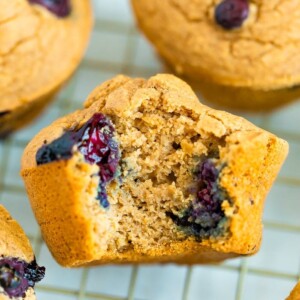 Blueberry muffin with a bite taken out of it on a cooling rack. A few whole blueberry muffins are around the bitten muffin.
