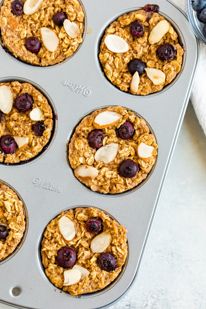 Muffin tin with blueberry baked oatmeal cups topped with almonds and blueberries.