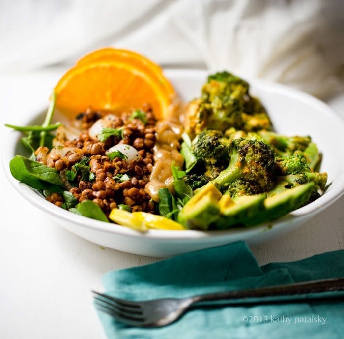 Broccoli + Lentil Power Plate in white shallow bowl on white countertop. Teal napkin with fork in the foreground.