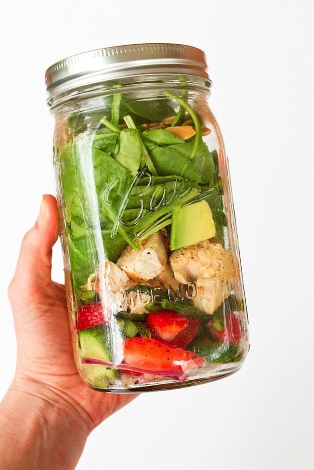 Hand holding a mason jar filled with salad ingredients. 